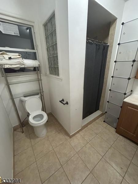 bathroom with walk in shower, vanity, tile patterned floors, and toilet