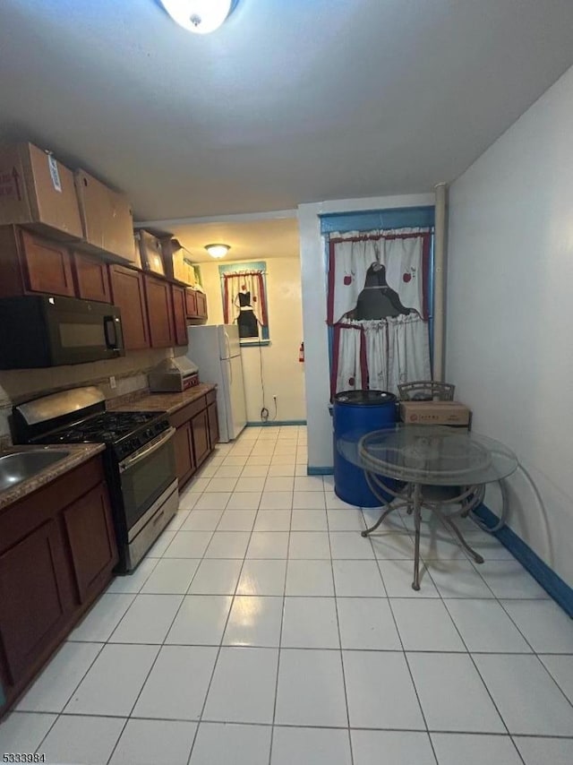 kitchen featuring white refrigerator, stainless steel range with gas stovetop, sink, and light tile patterned floors