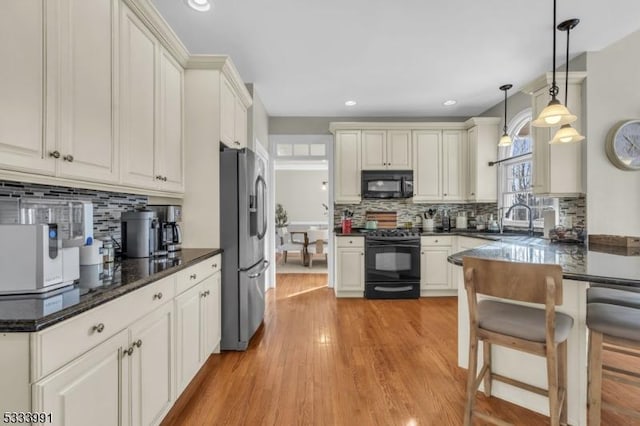 kitchen with pendant lighting, tasteful backsplash, sink, black appliances, and light wood-type flooring