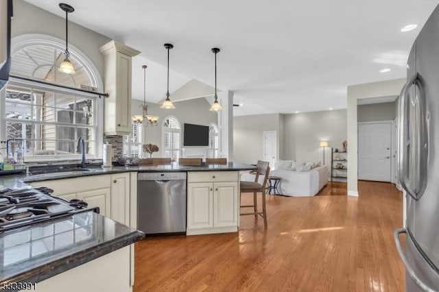 kitchen featuring vaulted ceiling, appliances with stainless steel finishes, decorative light fixtures, a breakfast bar area, and light hardwood / wood-style floors