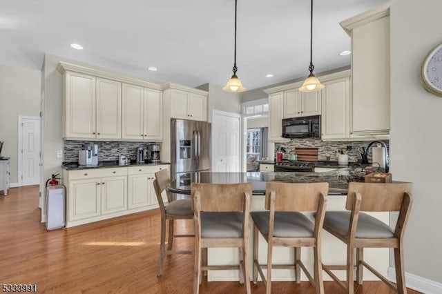 kitchen with hanging light fixtures, stainless steel appliances, light hardwood / wood-style floors, a kitchen bar, and cream cabinetry