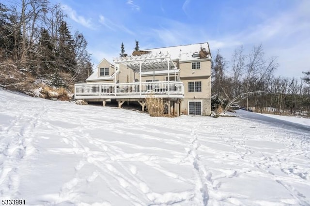 snow covered rear of property with a wooden deck and a pergola