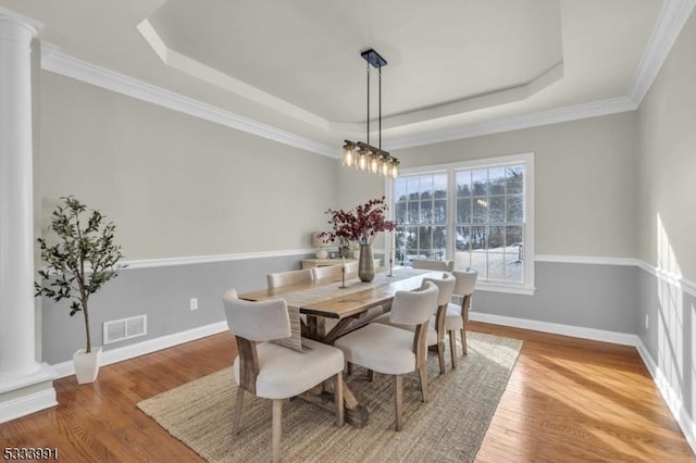 dining room featuring ornate columns, ornamental molding, light hardwood / wood-style flooring, and a tray ceiling