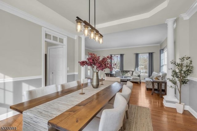 dining space featuring dark wood-type flooring, ornamental molding, a tray ceiling, and ornate columns