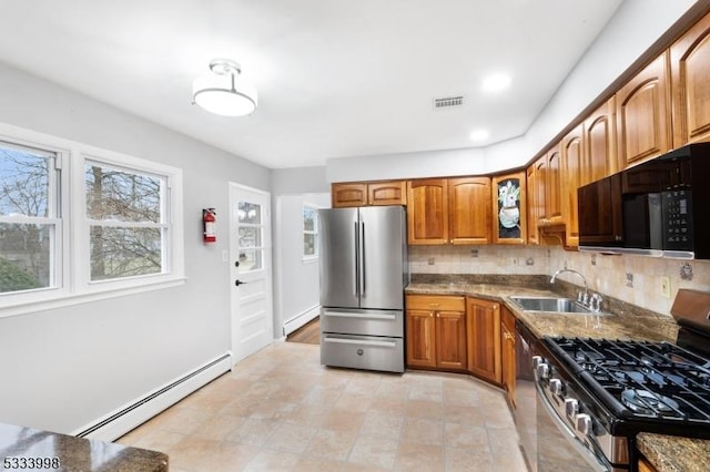 kitchen featuring stone countertops, sink, backsplash, a baseboard heating unit, and stainless steel appliances