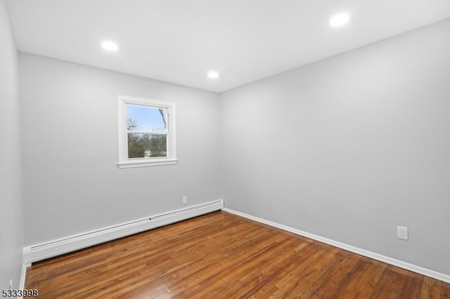 unfurnished room featuring a baseboard heating unit and hardwood / wood-style flooring