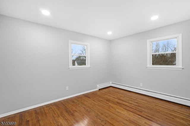 spare room with a baseboard heating unit, hardwood / wood-style flooring, and a wealth of natural light