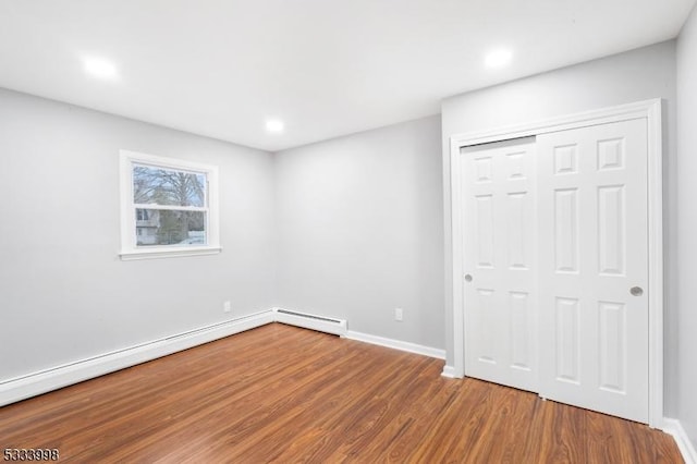 unfurnished bedroom featuring wood-type flooring, a closet, and a baseboard heating unit