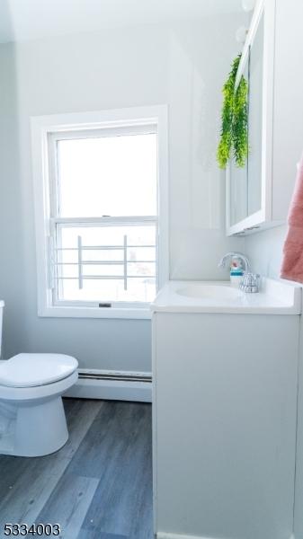 bathroom with a baseboard radiator, hardwood / wood-style floors, toilet, and vanity