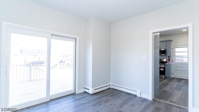 spare room featuring baseboard heating, dark wood-type flooring, and a wealth of natural light