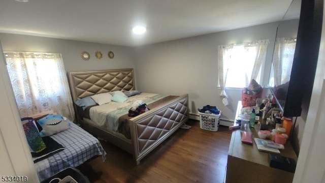 bedroom featuring a baseboard heating unit, dark wood-type flooring, and multiple windows