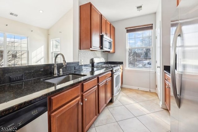 kitchen with vaulted ceiling, appliances with stainless steel finishes, tasteful backsplash, sink, and dark stone counters