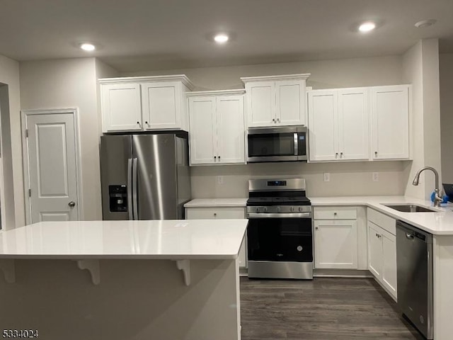 kitchen with a breakfast bar, sink, dark hardwood / wood-style flooring, stainless steel appliances, and white cabinets