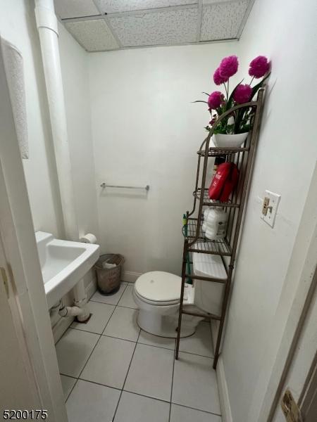 bathroom with a drop ceiling, toilet, and tile patterned flooring