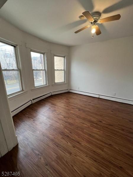 spare room featuring ceiling fan, a baseboard radiator, and dark wood-type flooring