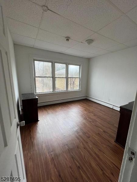 unfurnished room featuring baseboard heating, a drop ceiling, and dark hardwood / wood-style floors