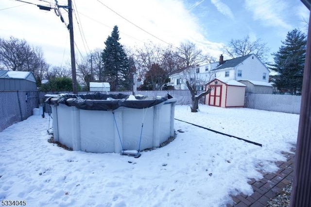 yard layered in snow featuring a storage shed and a covered pool