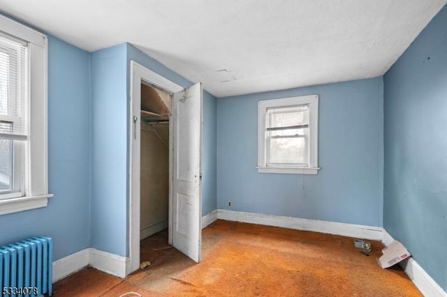 unfurnished bedroom featuring light colored carpet, multiple windows, radiator heating unit, and a closet