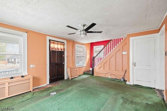 unfurnished living room featuring a textured ceiling, carpet flooring, radiator, and ceiling fan