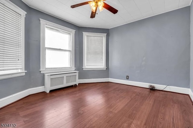 empty room with hardwood / wood-style floors, radiator heating unit, and ceiling fan