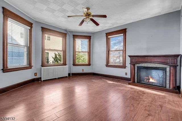 unfurnished living room featuring radiator, wood-type flooring, a fireplace, and ceiling fan