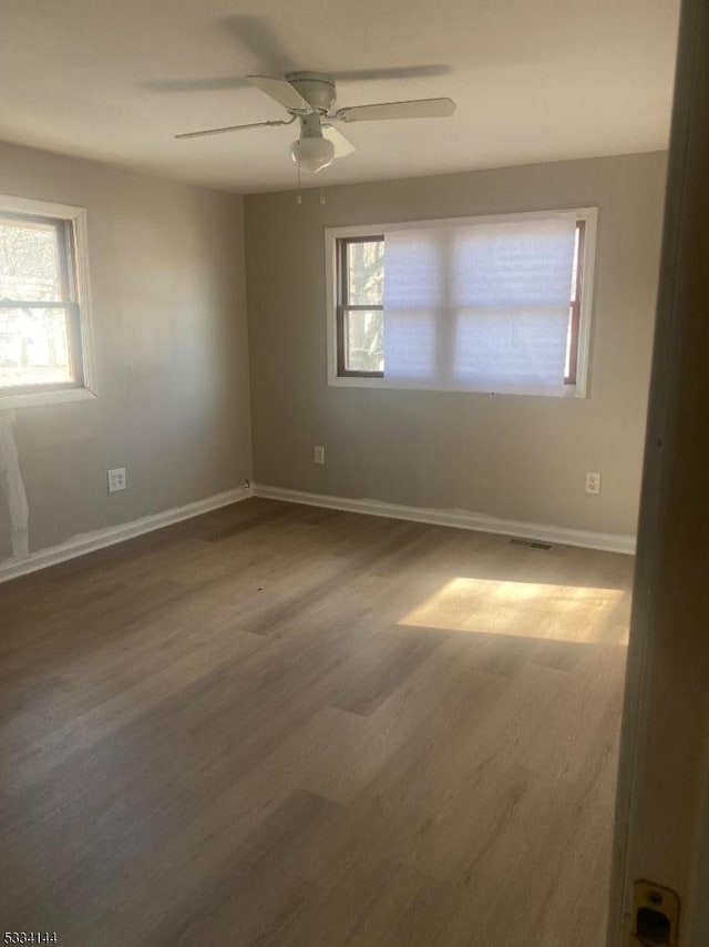 empty room featuring ceiling fan, dark wood-type flooring, and a healthy amount of sunlight