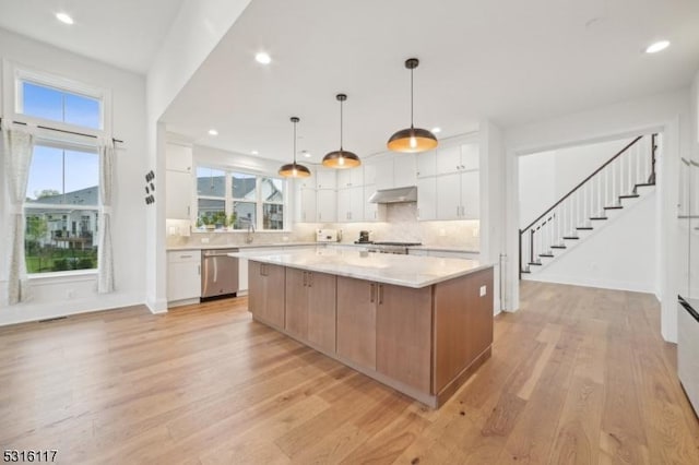 kitchen featuring pendant lighting, a spacious island, stainless steel dishwasher, and white cabinets