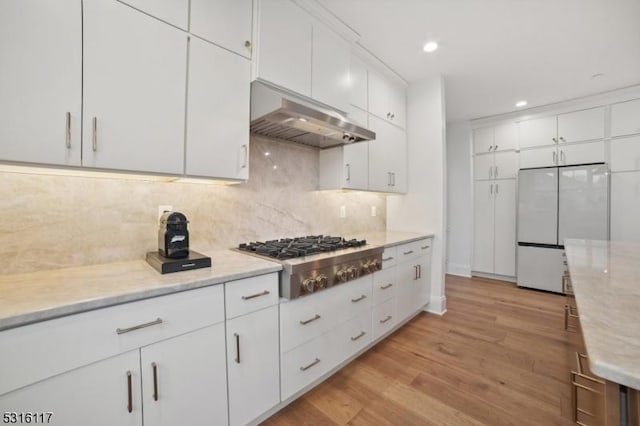 kitchen featuring light stone counters, light wood-type flooring, white fridge, stainless steel gas stovetop, and white cabinets