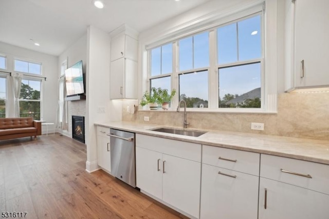 kitchen featuring sink, white cabinets, stainless steel dishwasher, light stone countertops, and light hardwood / wood-style flooring