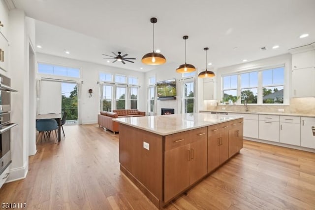 kitchen with hanging light fixtures, a kitchen island, a healthy amount of sunlight, light hardwood / wood-style floors, and white cabinets