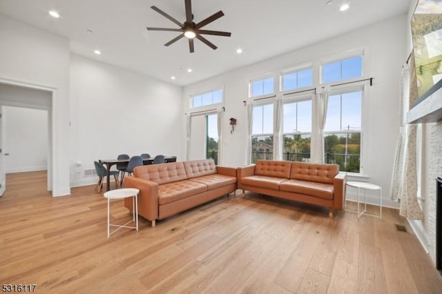 living room with a towering ceiling, a fireplace, a healthy amount of sunlight, and light wood-type flooring