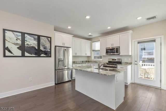 kitchen featuring dark wood-type flooring, light stone counters, an island with sink, stainless steel appliances, and white cabinets