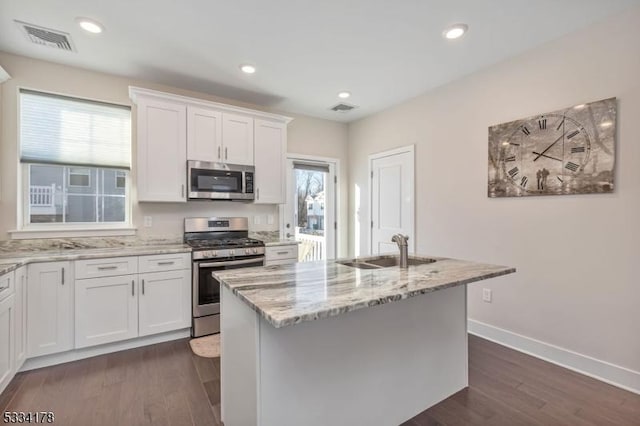 kitchen featuring appliances with stainless steel finishes, white cabinetry, sink, a kitchen island with sink, and light stone countertops