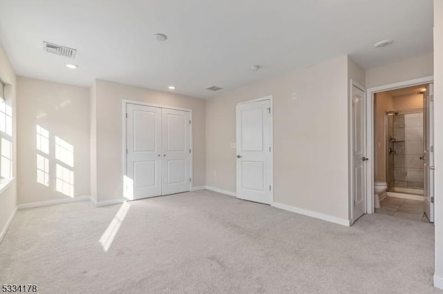 unfurnished bedroom with light colored carpet, ensuite bathroom, and a closet