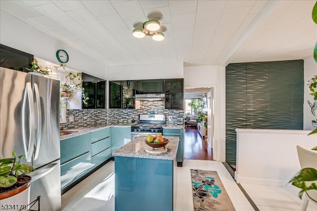 kitchen with light tile patterned floors, decorative backsplash, appliances with stainless steel finishes, a kitchen island, and under cabinet range hood