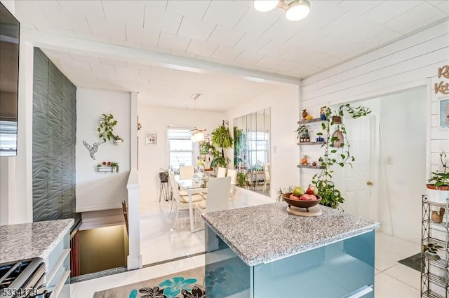 kitchen featuring light tile patterned floors, a center island, hanging light fixtures, stainless steel range oven, and beam ceiling