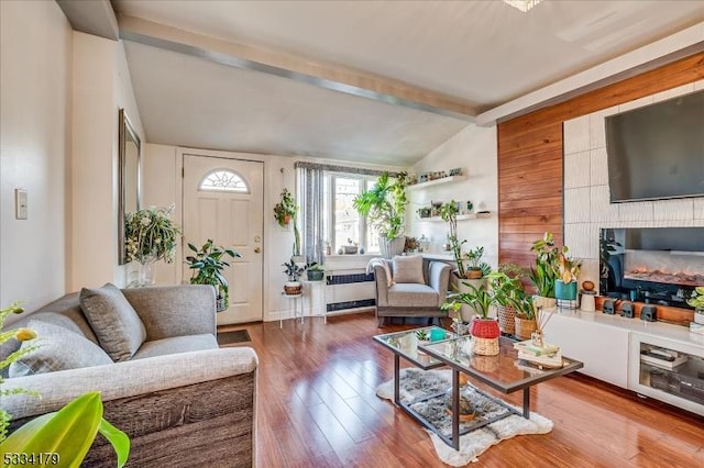 living room with lofted ceiling with beams, radiator, wood finished floors, and a glass covered fireplace