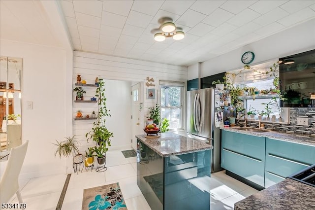 kitchen with freestanding refrigerator, a sink, blue cabinetry, and light tile patterned floors