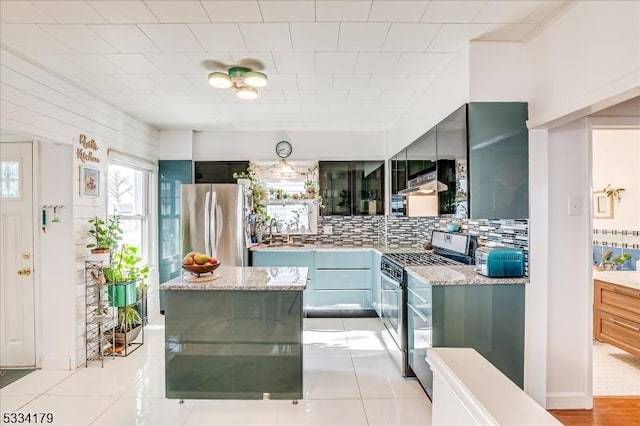 kitchen featuring light tile patterned floors, decorative backsplash, appliances with stainless steel finishes, a sink, and light stone countertops