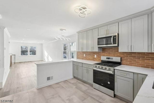 kitchen with light stone counters, stainless steel appliances, gray cabinets, and backsplash