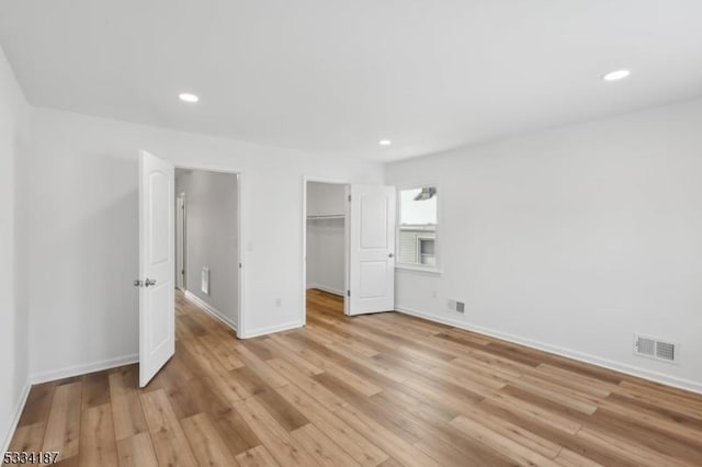 unfurnished bedroom with a spacious closet, a closet, and light wood-type flooring