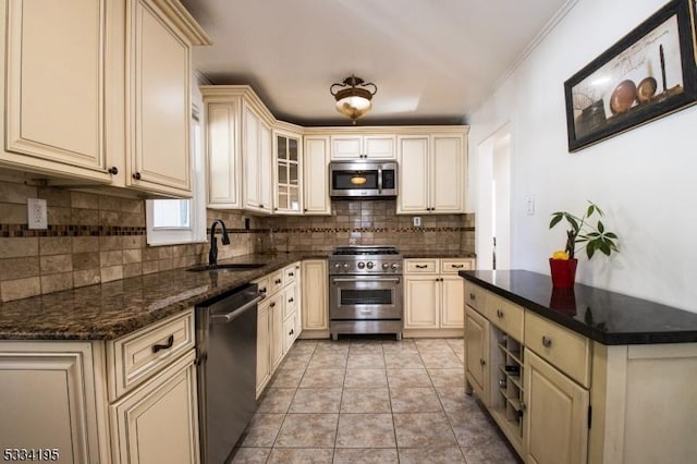 kitchen featuring light tile patterned flooring, sink, dark stone counters, stainless steel appliances, and cream cabinetry