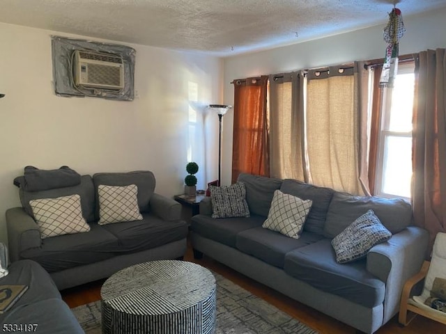 living room featuring a textured ceiling, dark hardwood / wood-style floors, an AC wall unit, and a healthy amount of sunlight