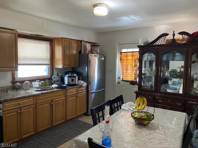 kitchen featuring light tile patterned flooring, stainless steel fridge, light stone countertops, and sink