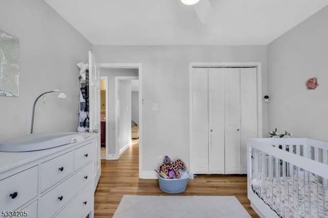 bedroom featuring a crib, a closet, ceiling fan, and light wood-type flooring