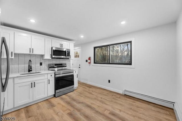 kitchen featuring sink, a baseboard radiator, stainless steel appliances, and white cabinets