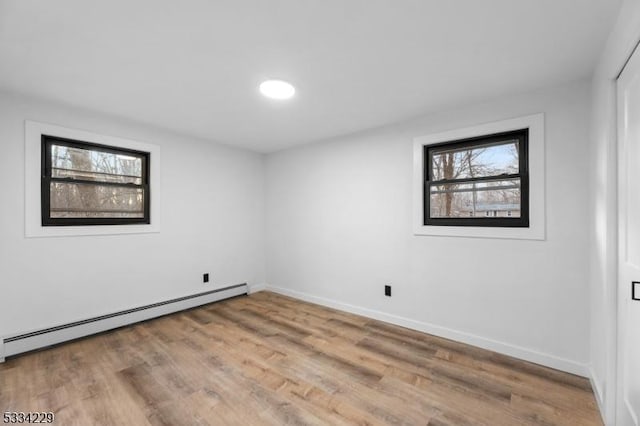 empty room with a baseboard heating unit, a healthy amount of sunlight, and light wood-type flooring