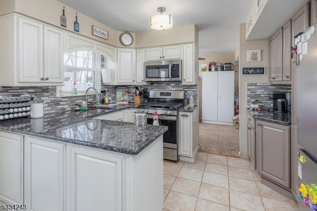 kitchen with appliances with stainless steel finishes, white cabinetry, sink, light tile patterned floors, and kitchen peninsula