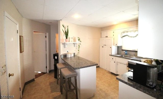 kitchen featuring sink, white cabinets, a kitchen bar, a drop ceiling, and kitchen peninsula