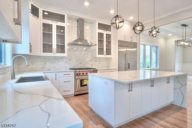 kitchen featuring a large island, wall chimney range hood, white cabinetry, hanging light fixtures, and premium appliances